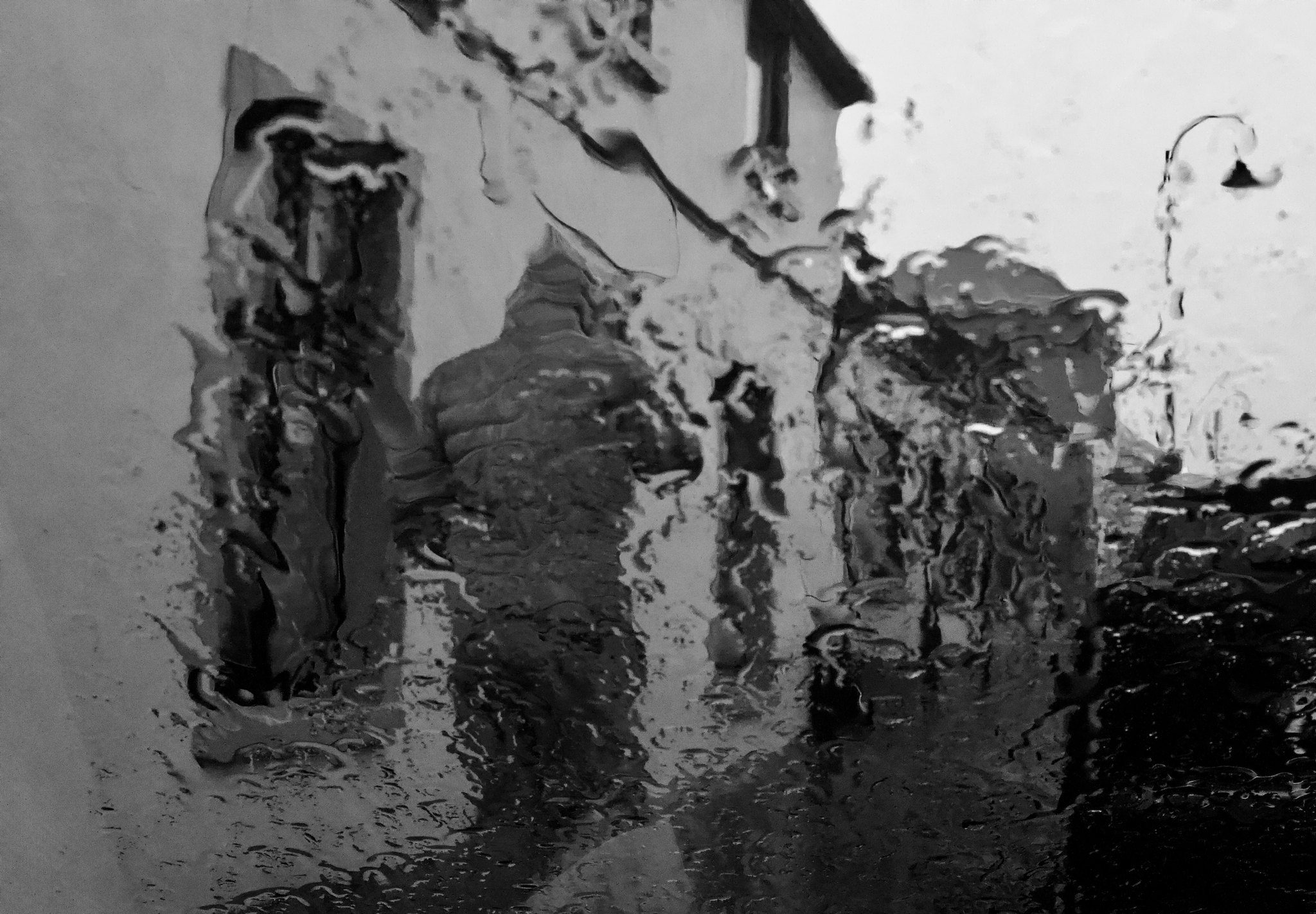 Abstract black and white photograph of a street seen through a rain-streaked window, a passer-by and a street lamp blurred by running raindrops, County Kerry